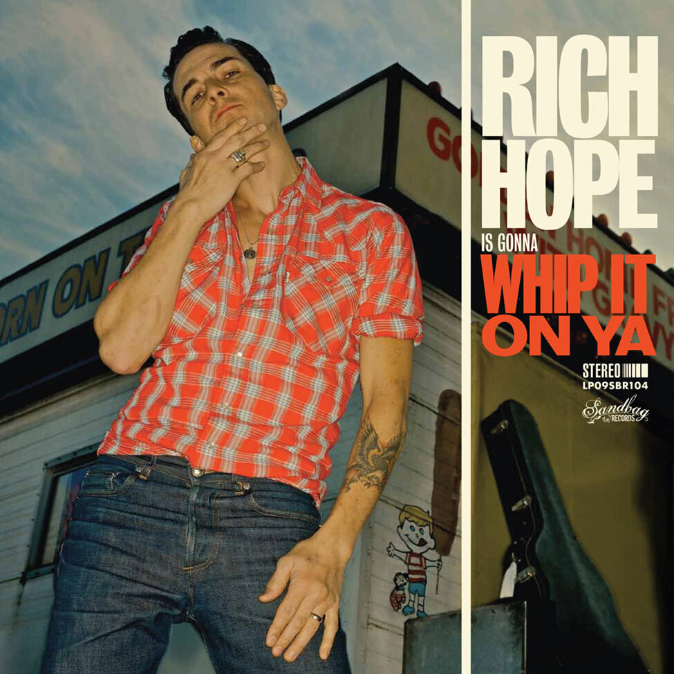 Album Cover Title Rich Hope Is Gonna Whip It On Ya artist standing in foreground with hand to his chin guitar case leaning against old wooden food stand behind him