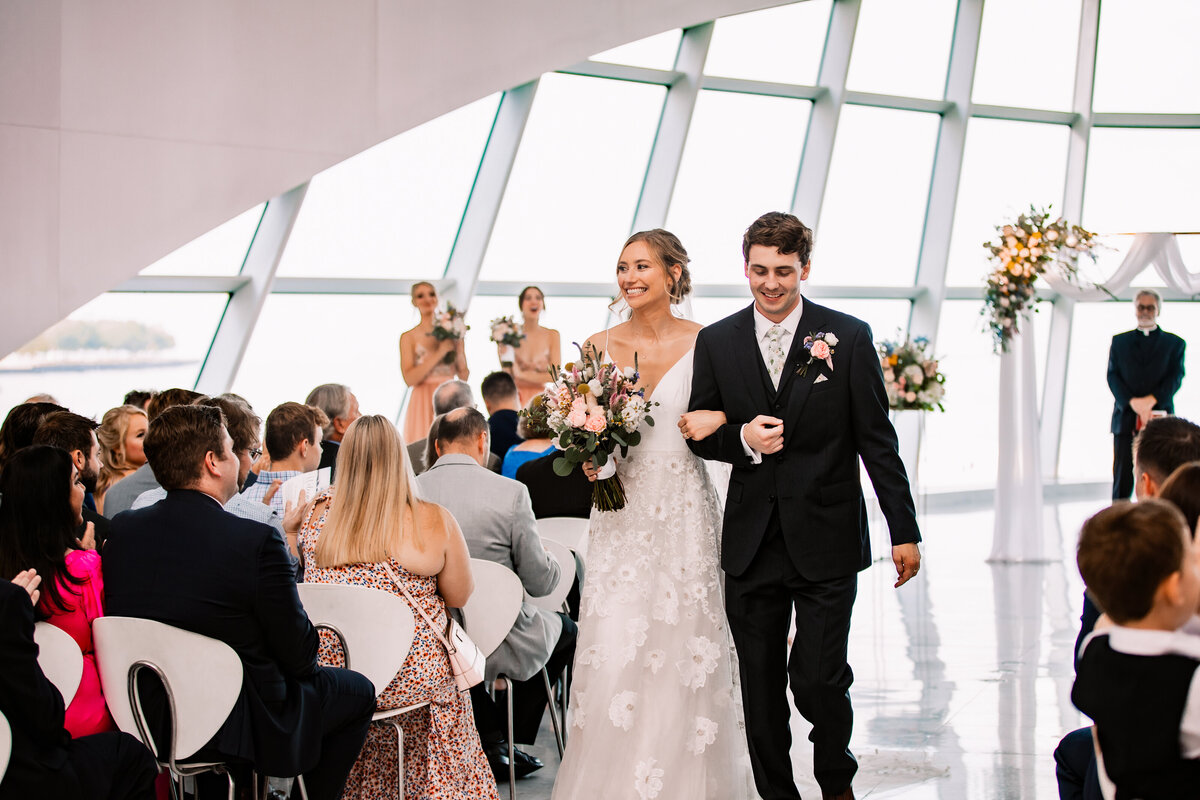 A bride and groom happily walk back up the aisle locking arms after their ceremony