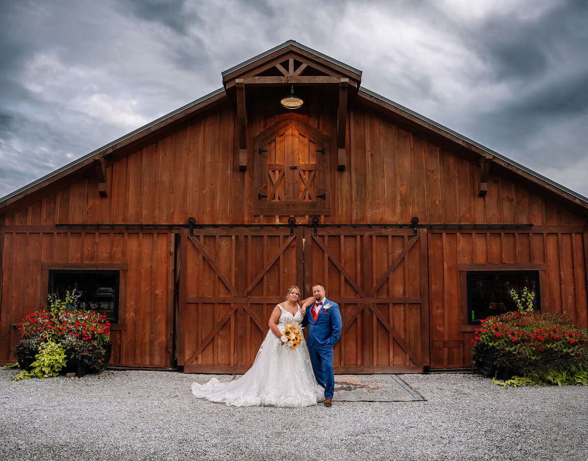 Bride and groom posing together in front of a large barn under cloudy skies