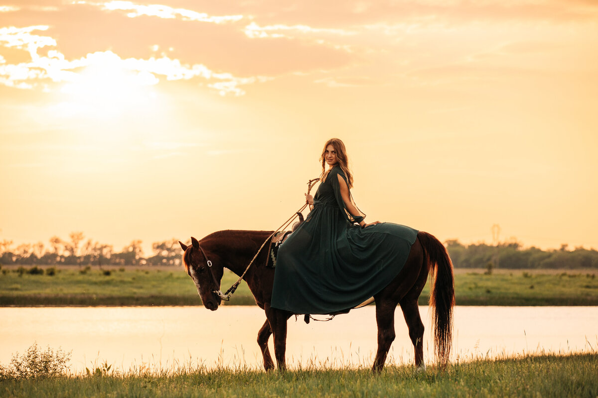 woman in emerald dress on her horse by a lake