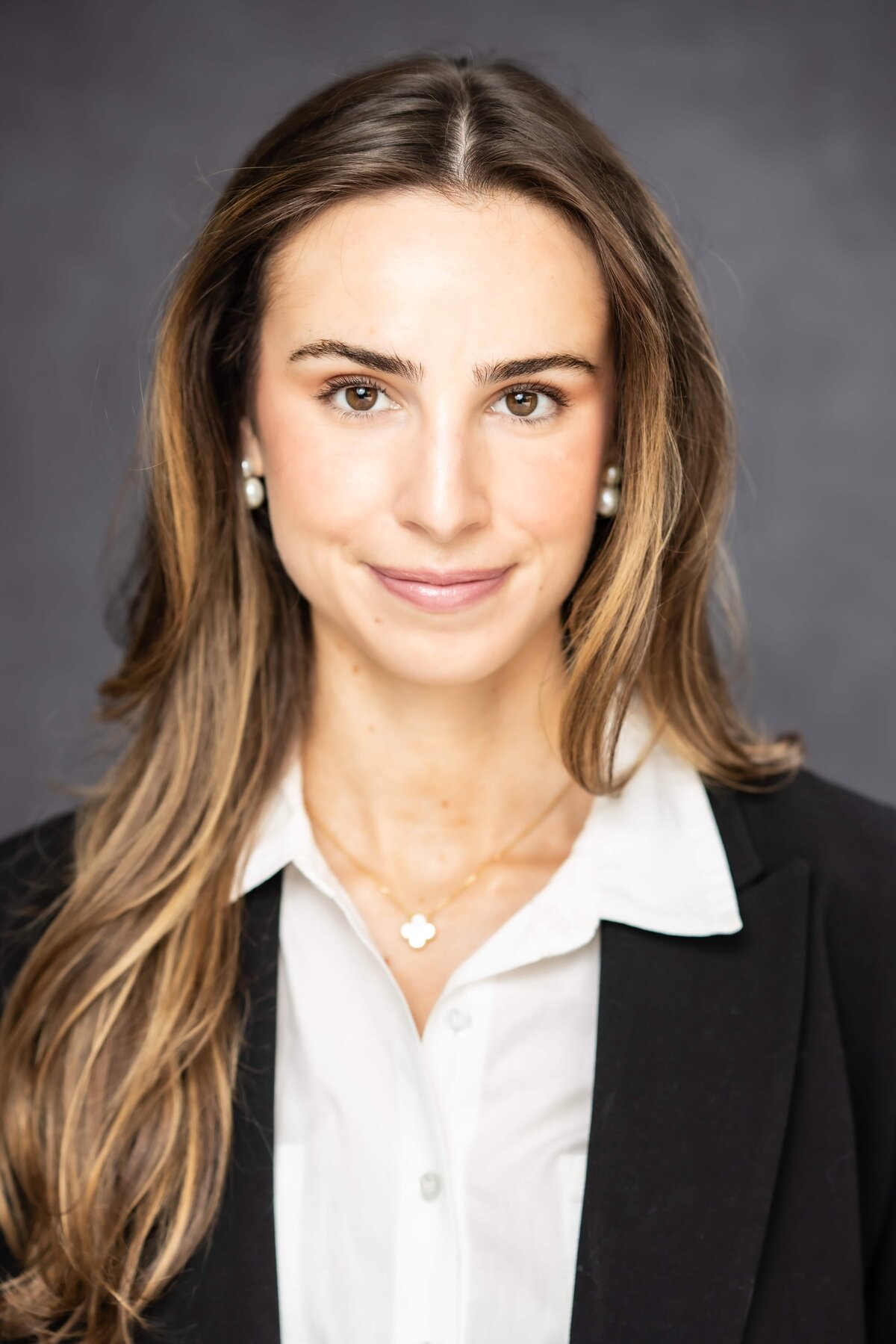 Portrait of a young woman with a bright smile and long hair in a dark blazer and a white shirt posing for a headshot