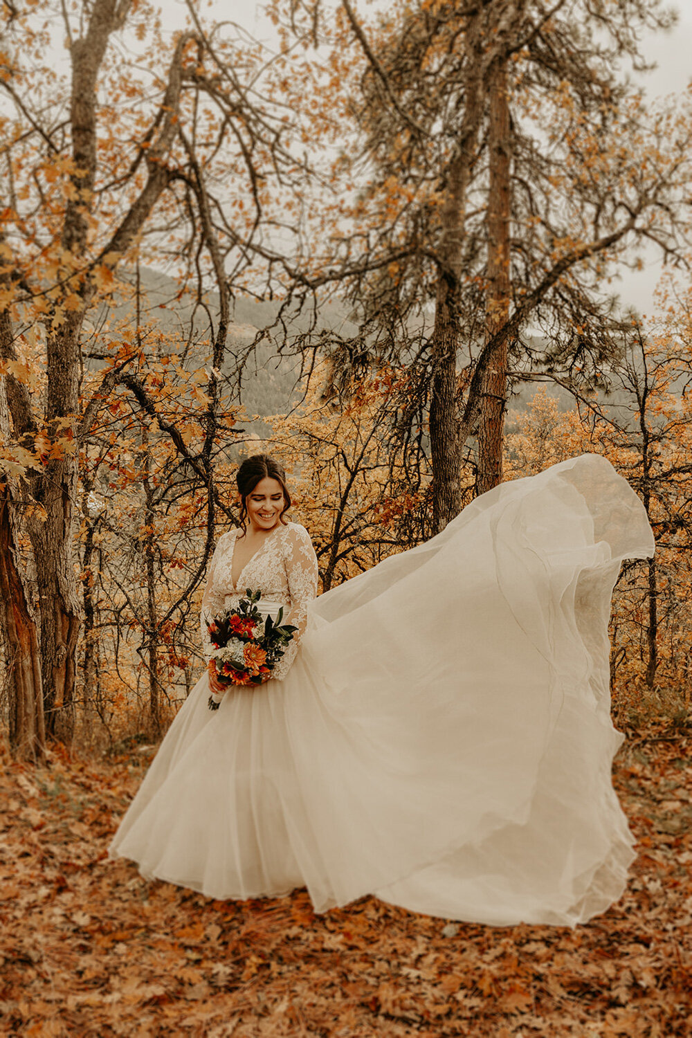 Bride wearing her wedding gown and holding her bouquet surrounded by trees