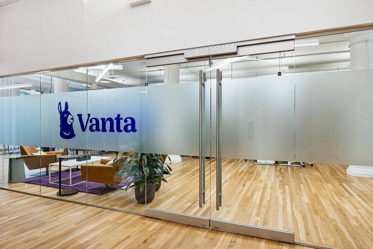 Wide glass office entryway with frosted panels and bold blue logo above polished wood flooring.