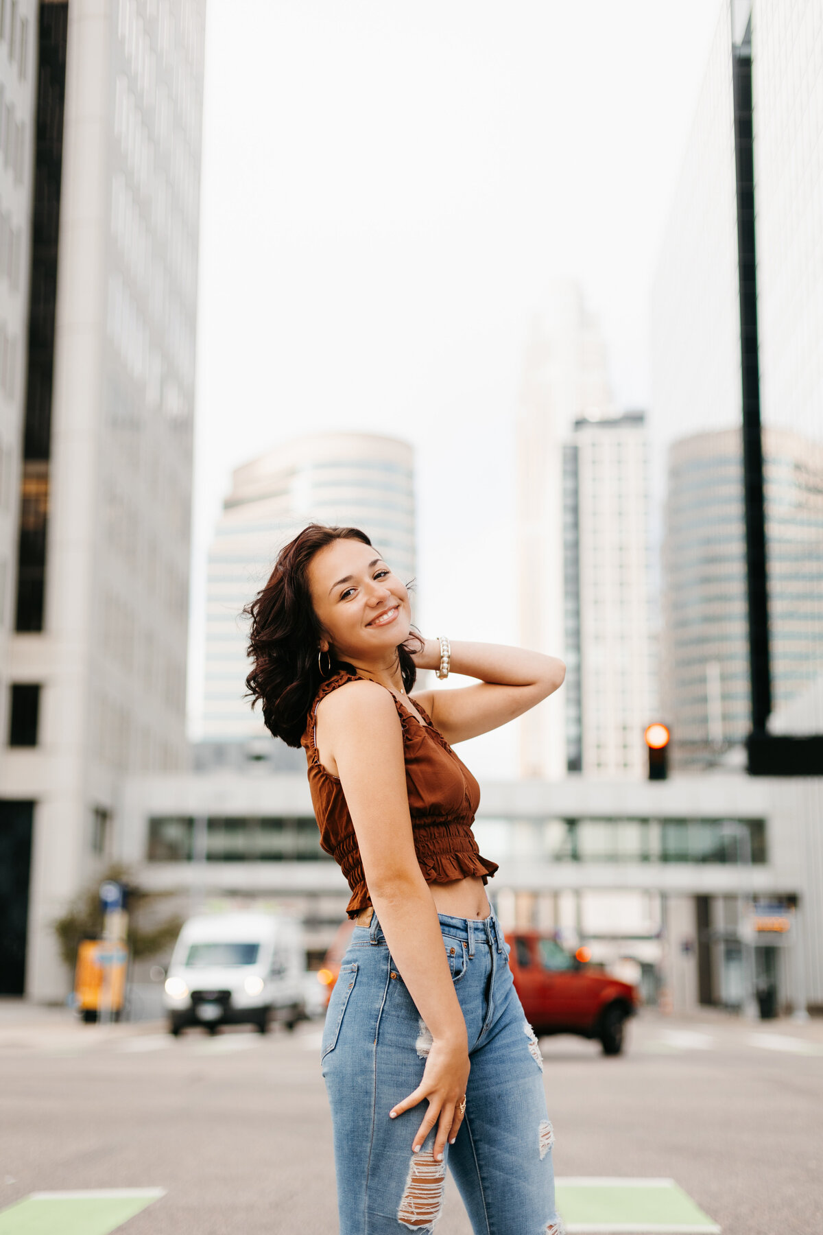 Senior girl in a brown top and jeans posing in front of a busy city street
