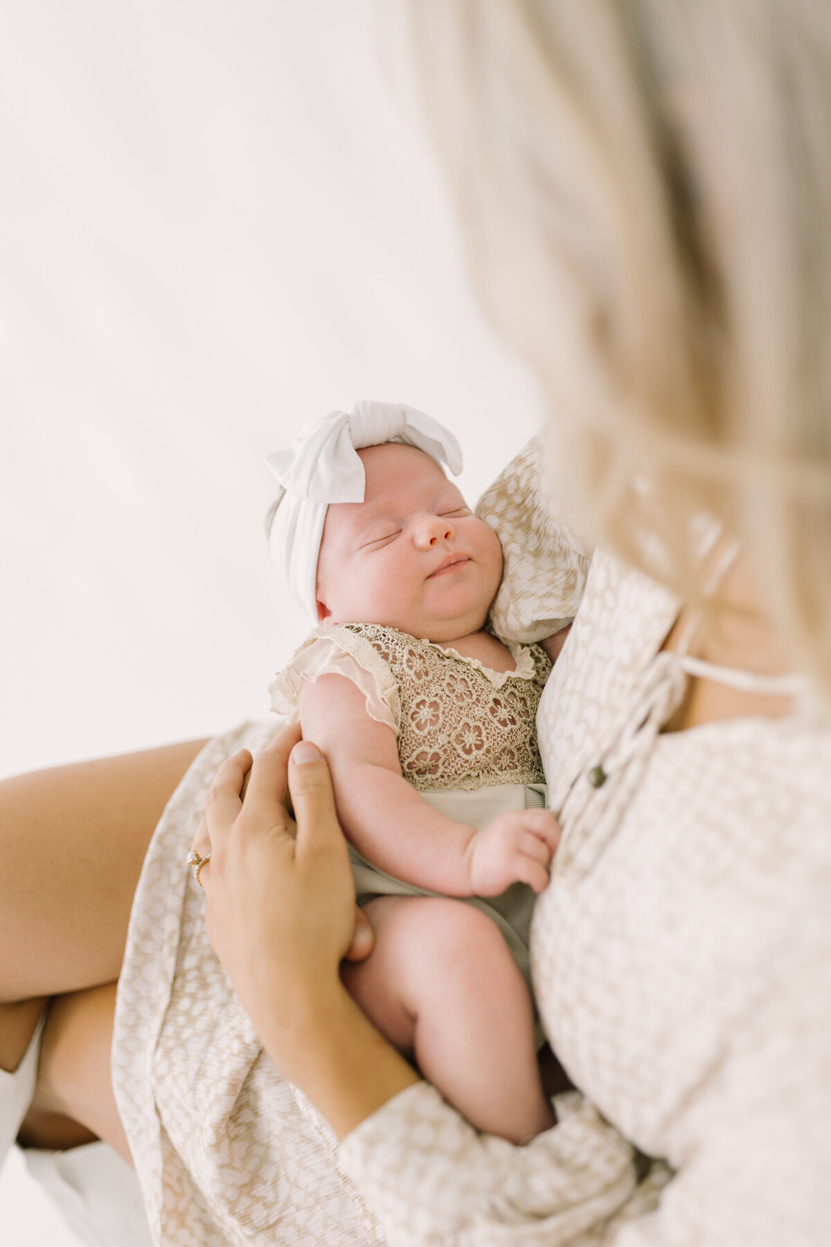 A mother cradling her newborn baby girl in a soft, light-filled studio — Raleigh portrait photography.