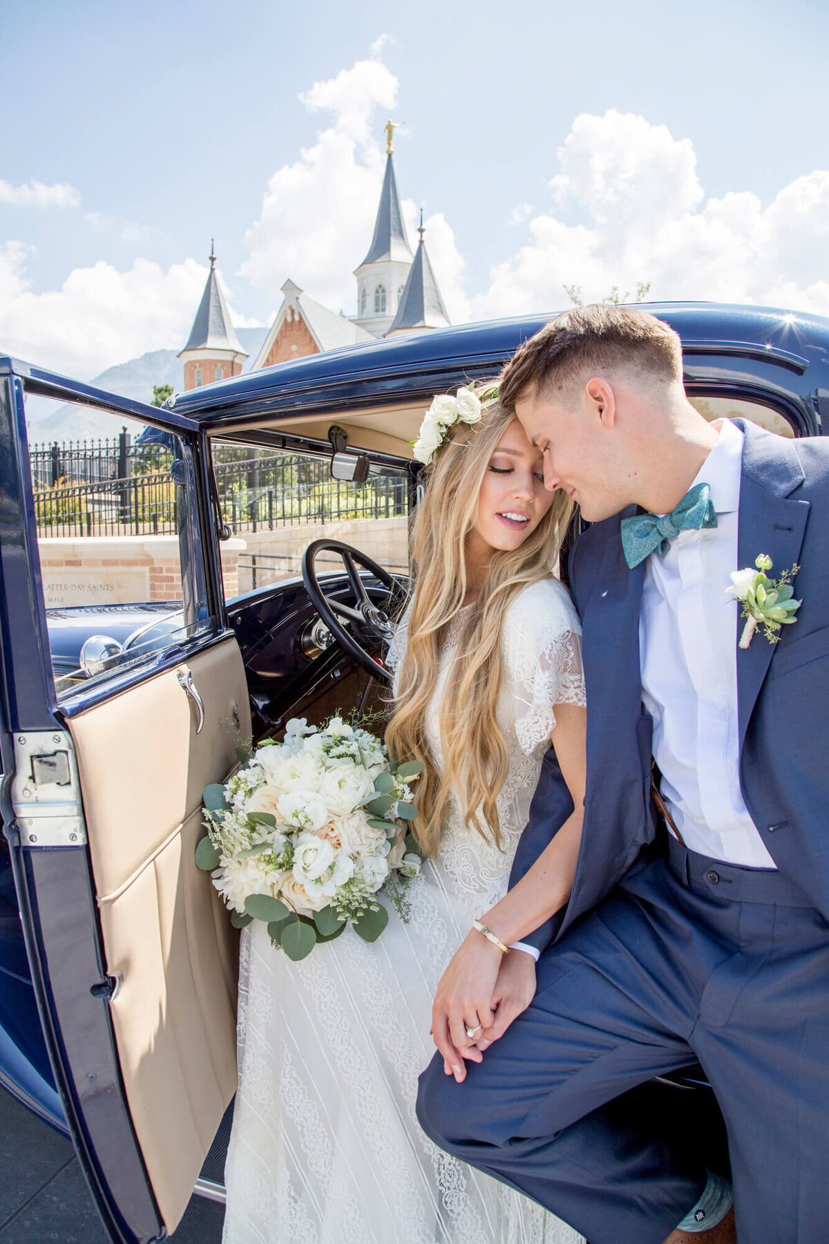 bride and groom holding hands in front of a vintage blue car on a sunny day