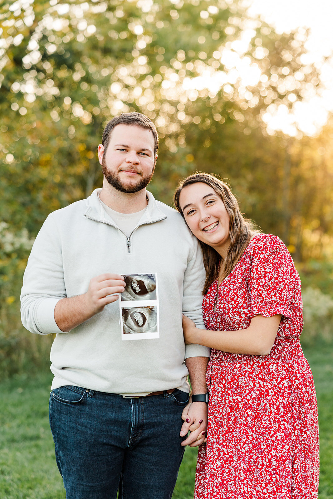 Pregnant couple standing outside holding sonogram images