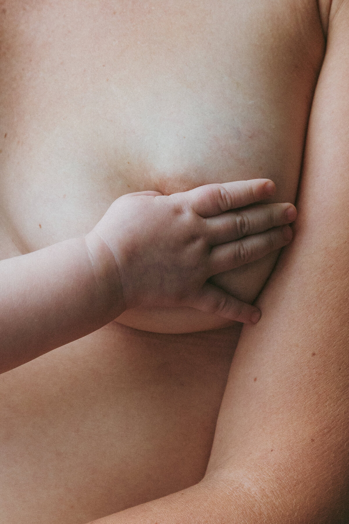 Closeup of a baby’s hand on mother’s breast. Intimate family photography capturing the bond in Portland and Nashville.