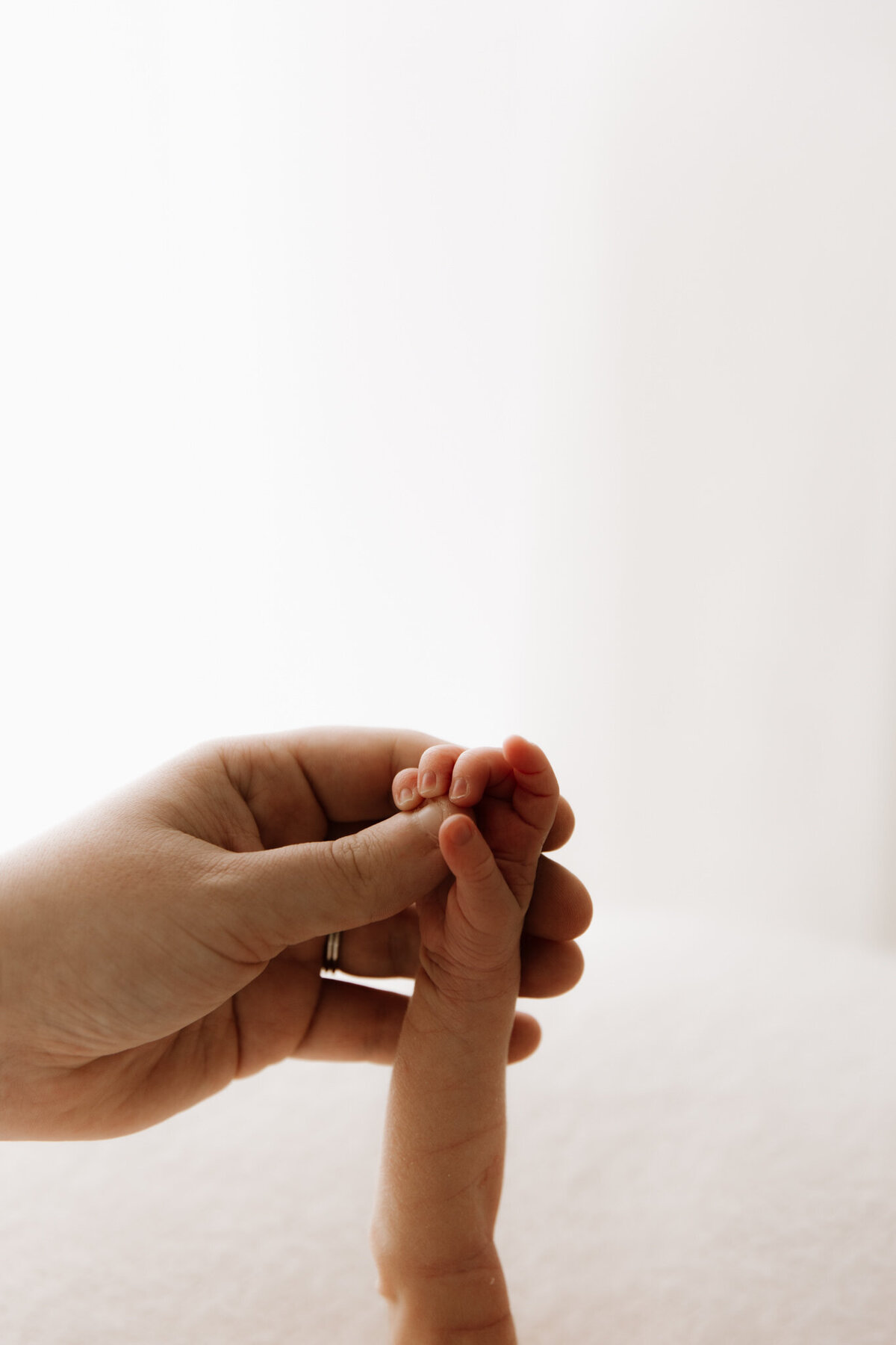A close-up of a parent gently holding their newborn's tiny hand against a soft, creamy backdrop. The image captures the tenderness and delicate connection between mother and baby, evoking warmth, love, and trust.