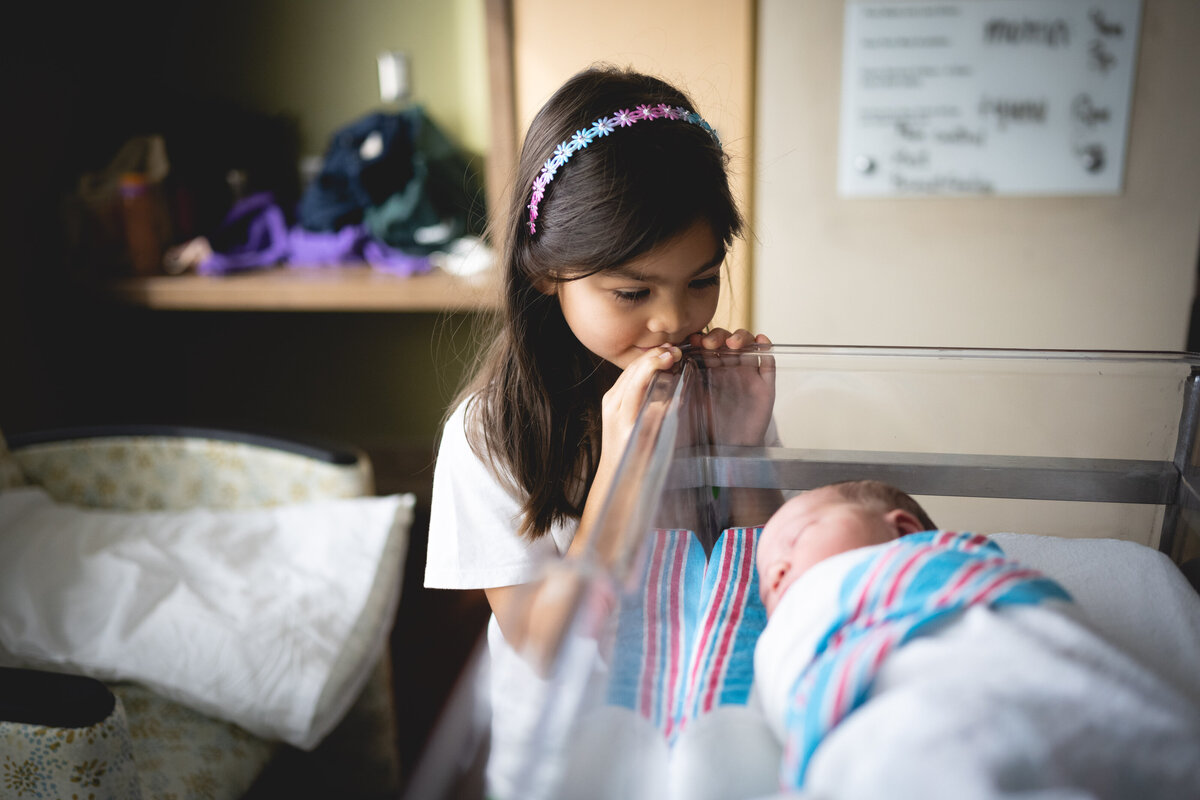older sister looking at newborn baby in hospital bassinet
