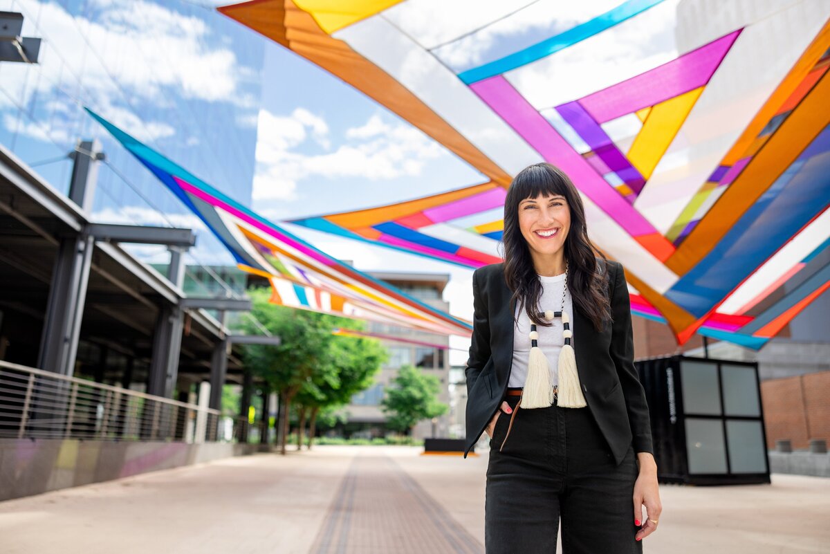 Woman on black outfit poses next to art installation she curated