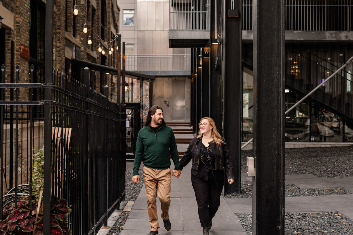 Engaged couple holding hands walking through Winnipeg's Exchange District