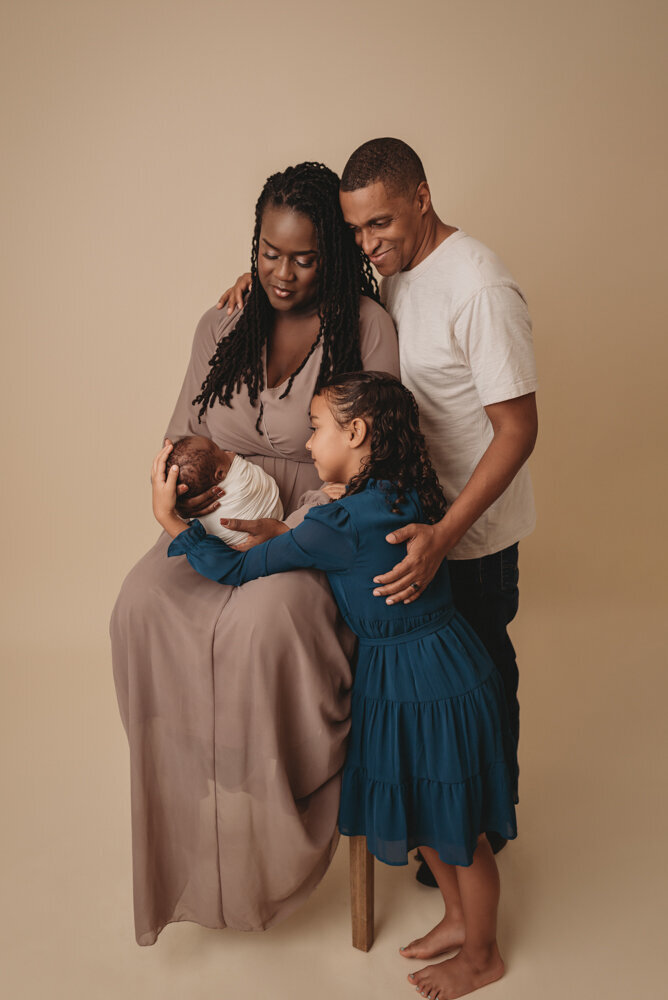 Newborn photos with Atlanta, Georgia newborn photographer of sleeping baby boy with hands under chin wrapped in cream swaddle being held by his mom, dad and big sister.