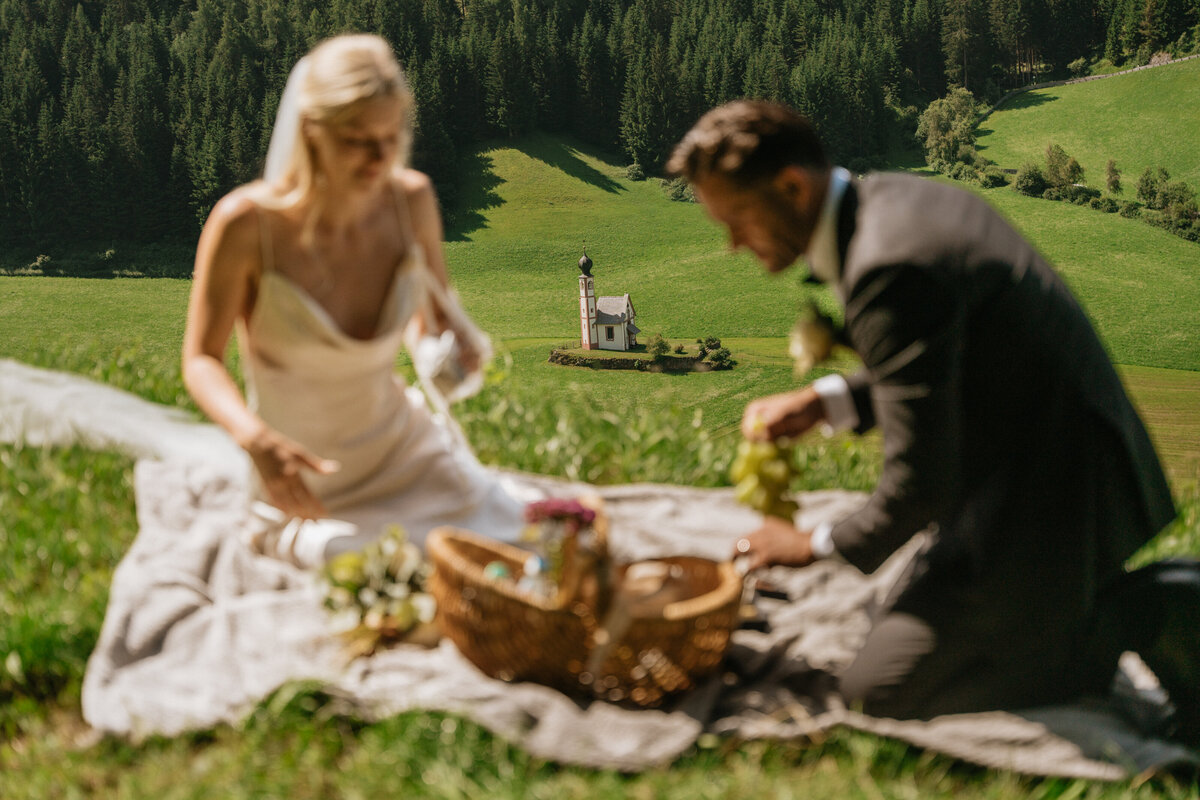 Bride and groom enjoying picnic on blanket in Val di Funes