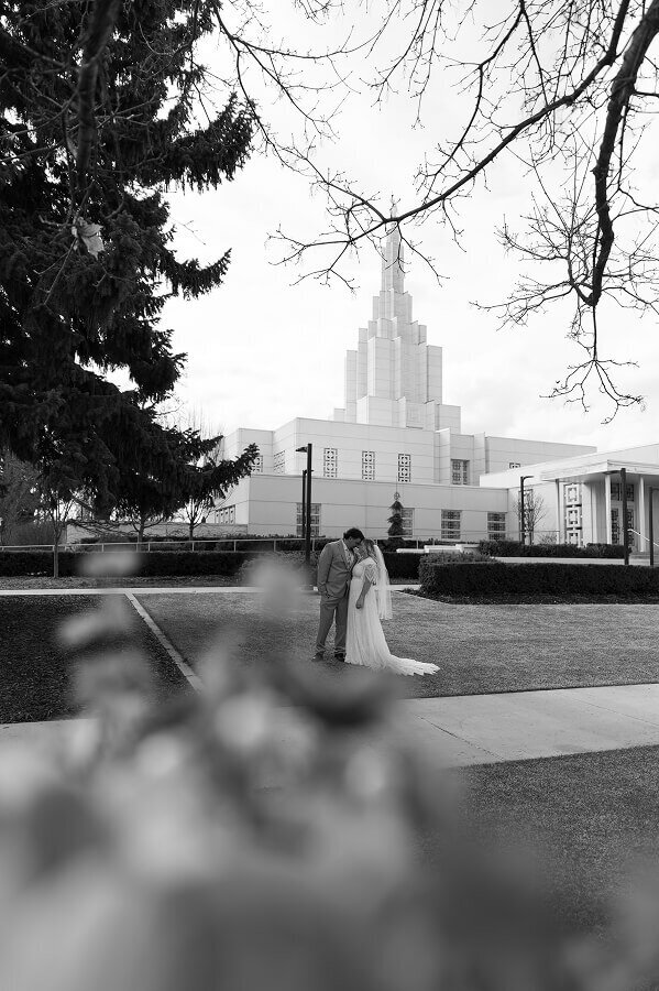 A timeless black and white photo of a bride and groom standing in the lawn in front of a LDS temple on their wedding day.