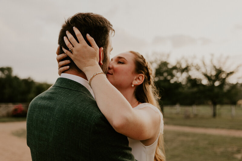 Mariés se faisant tendrement un bisou dans un cadre de nature. Focus sur le visage de la mariée, le marié lui est de 3/4 dos. Photo par Laura Termeau Photographie.