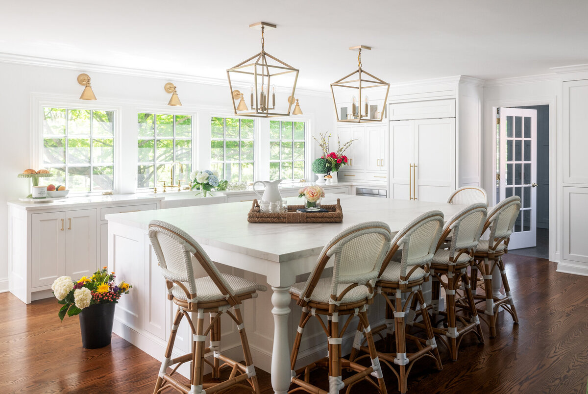 Bright white kitchen with gold light fixtures and wood and light whicker chairs