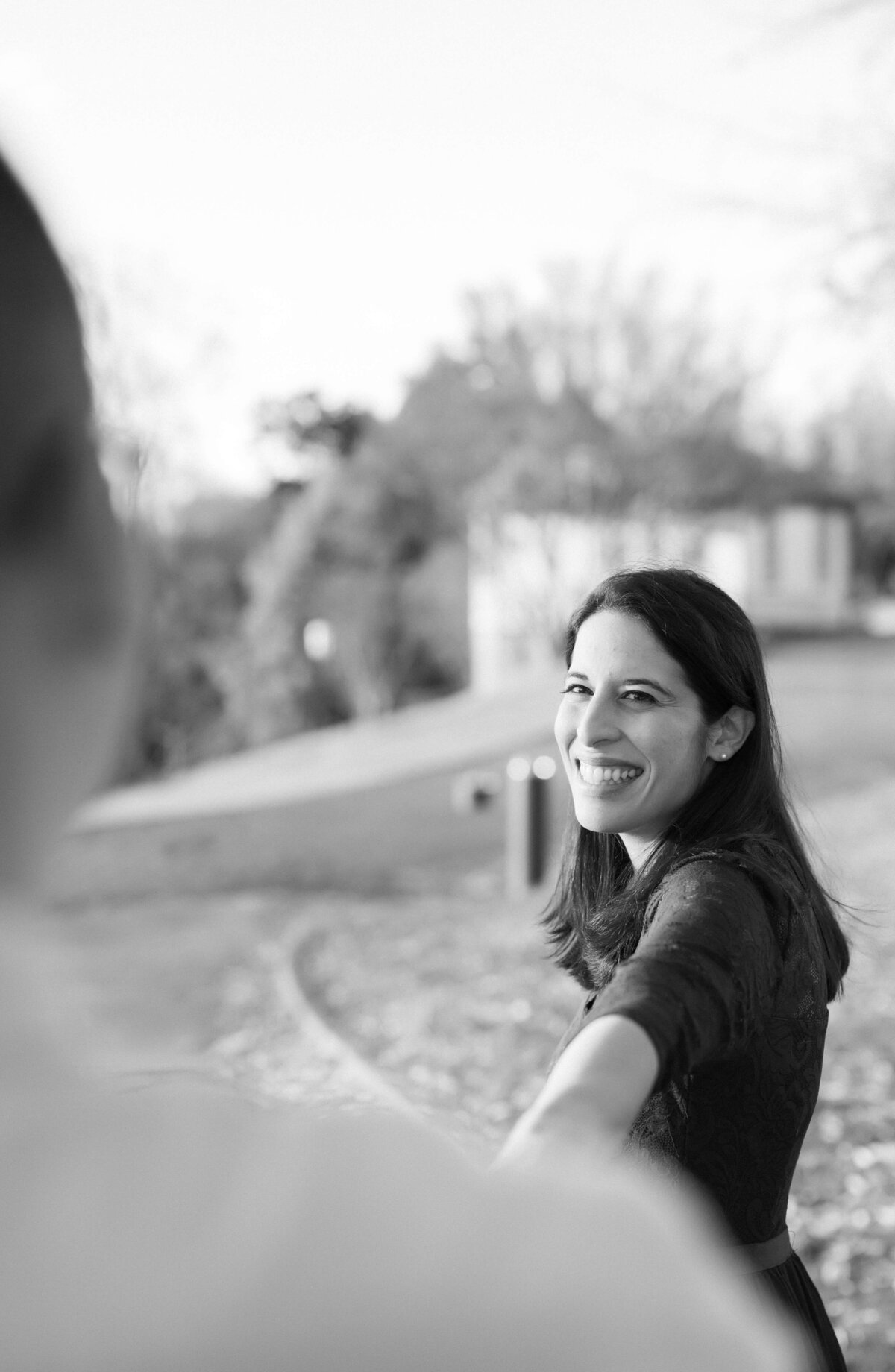 black and white engagement photo with woman holding mans hand and leading him through a trail at a park in Richmond