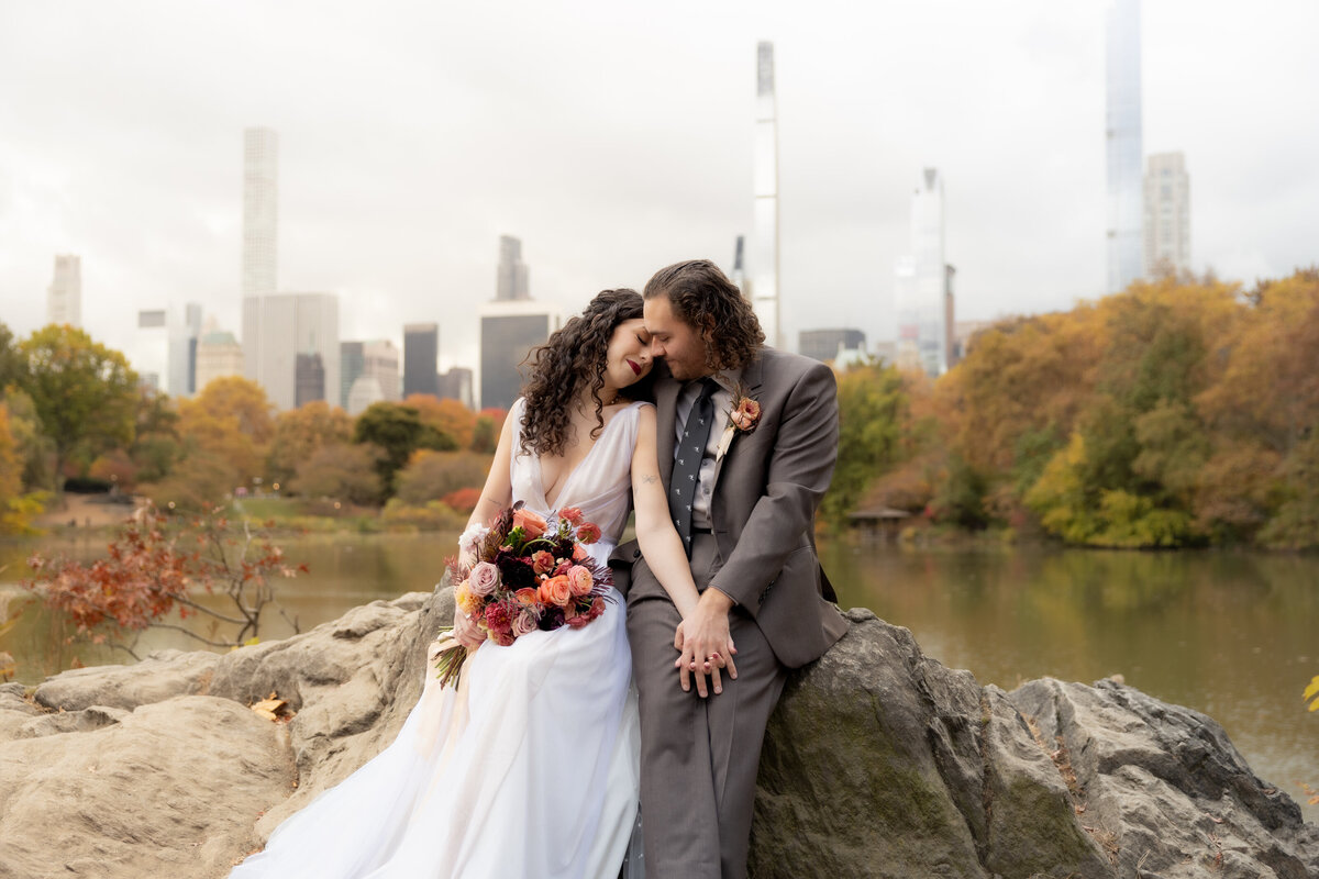 The couple standing close together surrounded by Central Park’s glowing fall foliage.