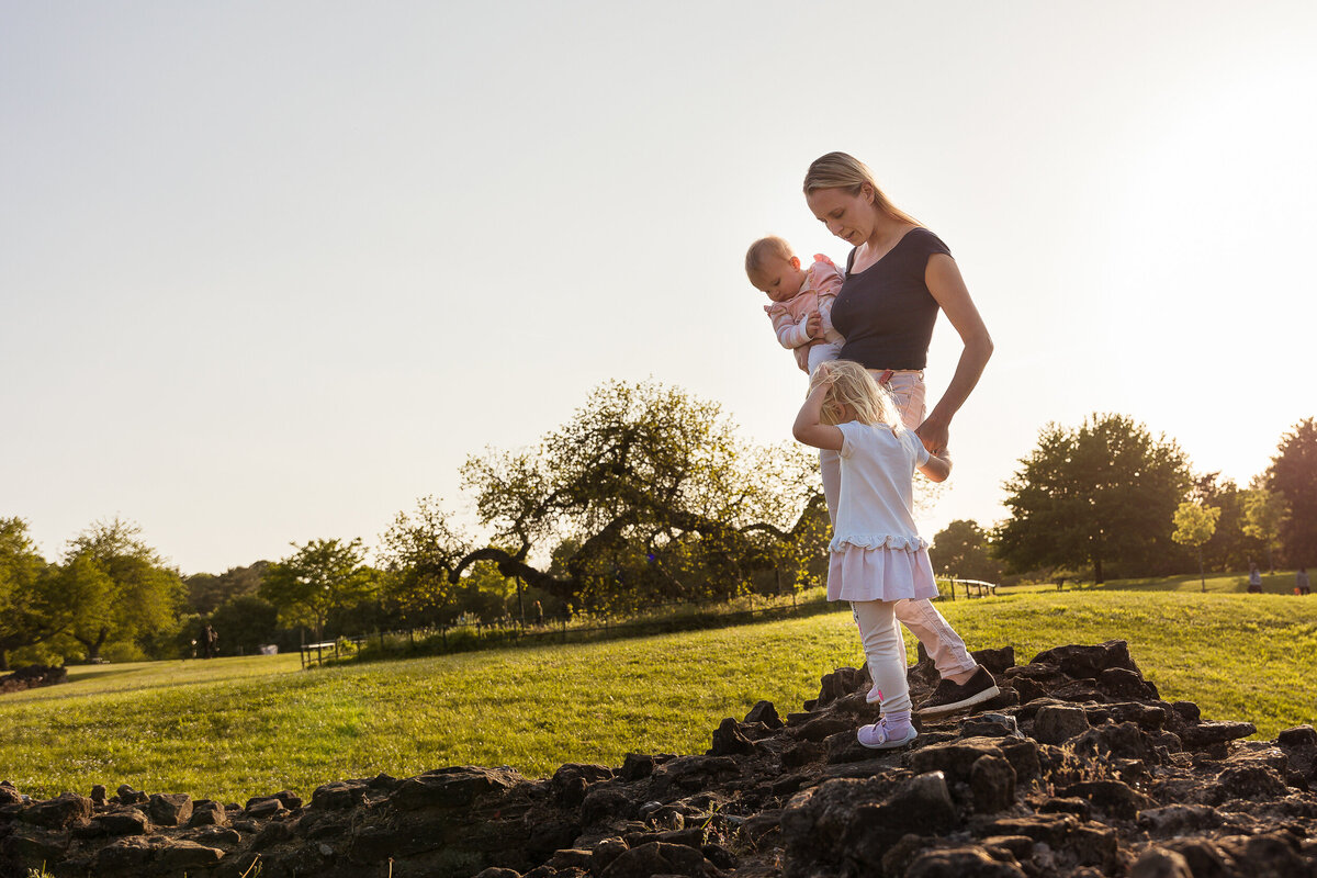 A mother and daughter posing for a photography session on top of a rock in a park.