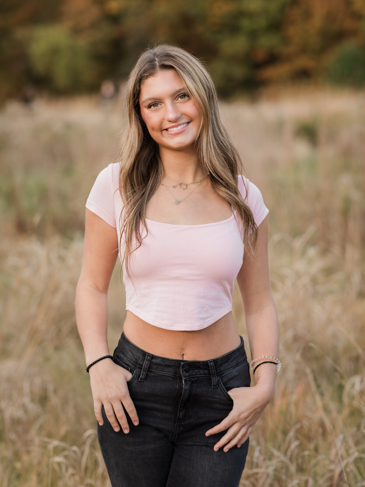 senior girl in pink top posing for senior photos in field at Westcreek Reservation in Parma, Ohio 