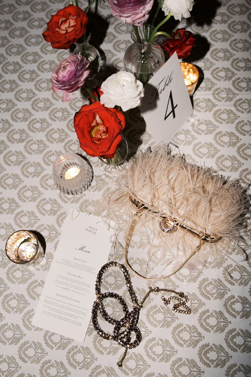 Wedding reception tablescape featuring bright florals, feather bridal bag, jewelry, and printed menu at Old Edwards Inn.