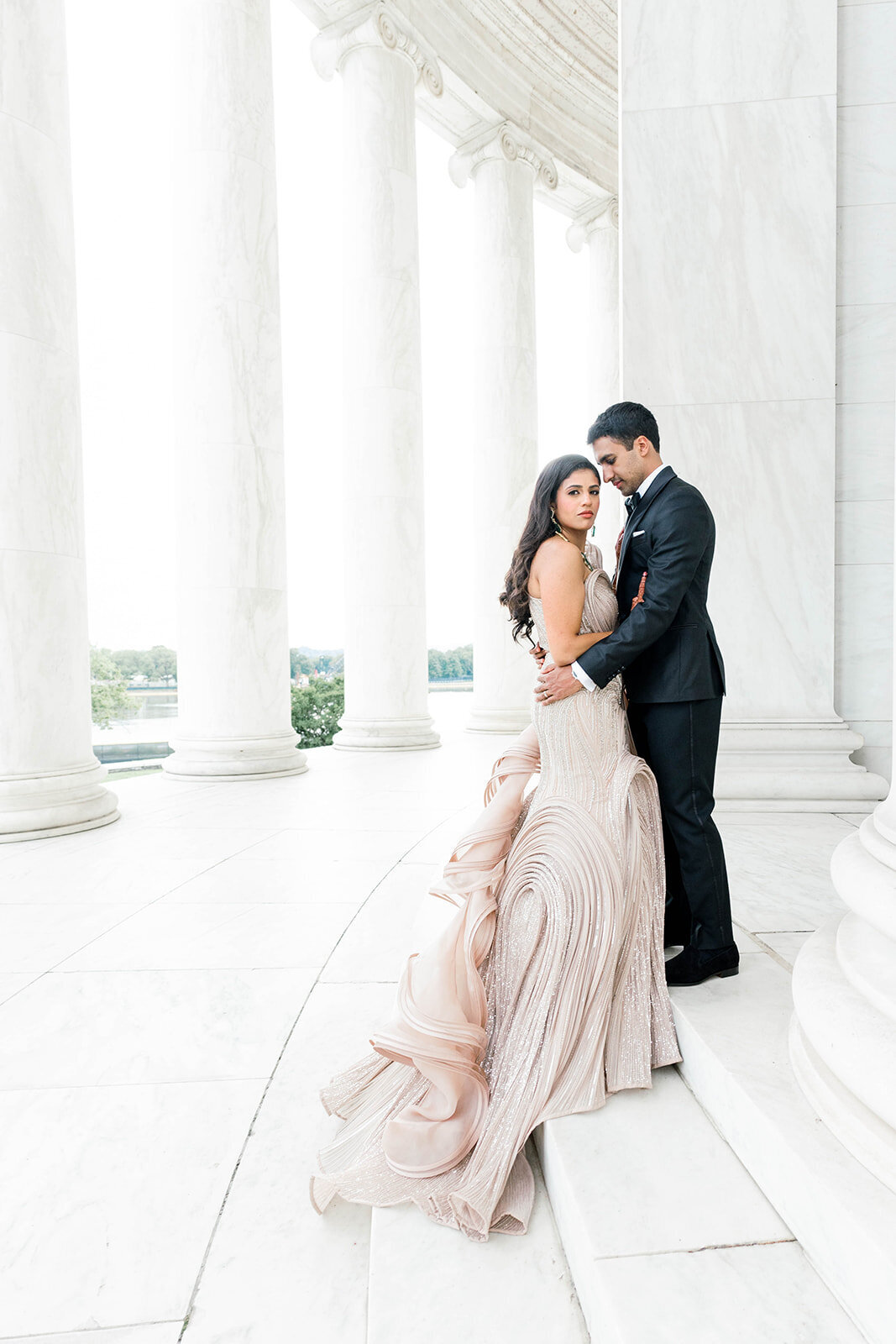 Bride in a champagne sculptural gown and groom in a classic black tux pose at the Jefferson Memorial in Washington DC during a luxury wedding, photographed by Mari Harsan Studios.