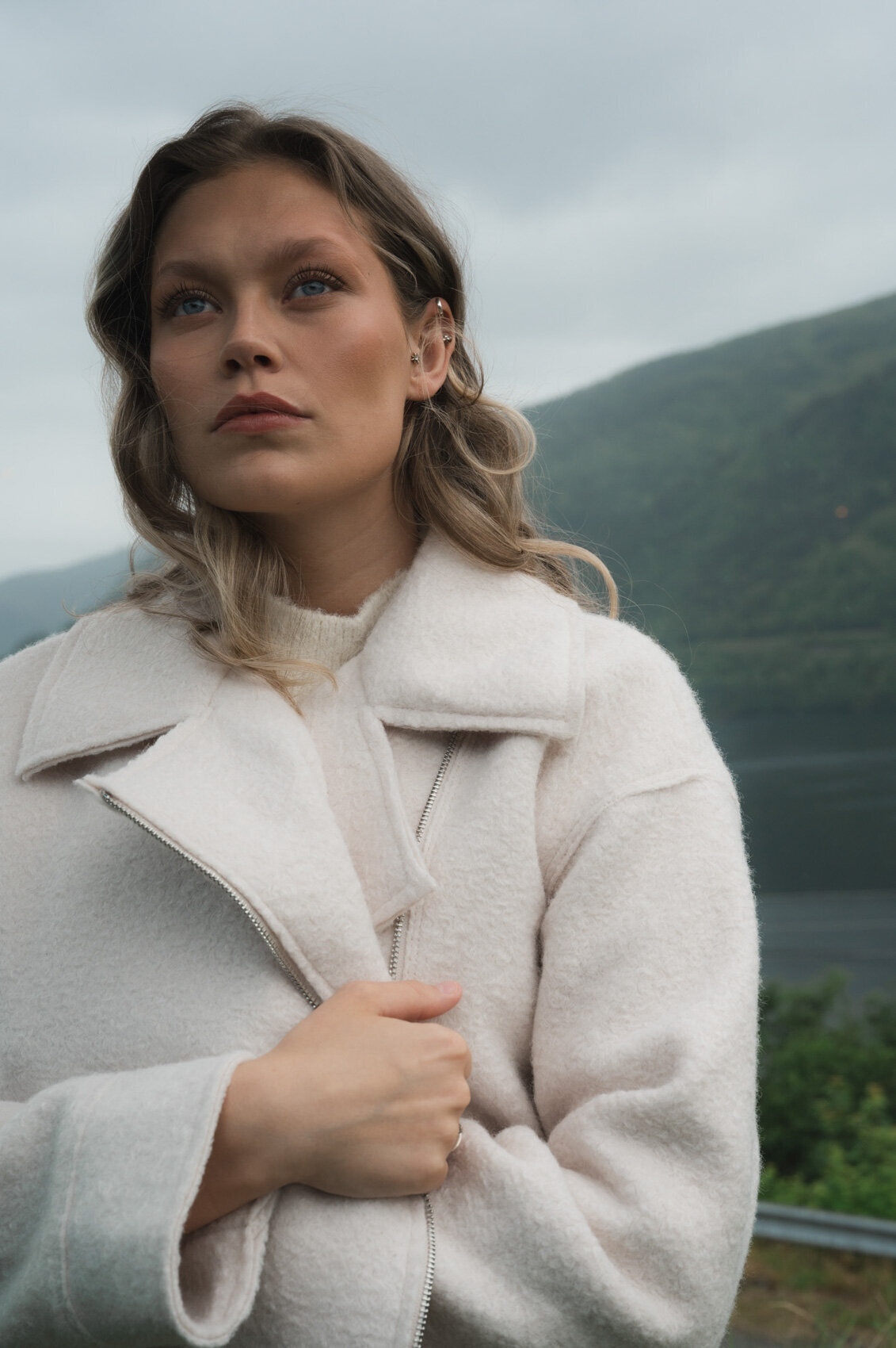 Fashion model standing in the Scandinavian landscape in white coat