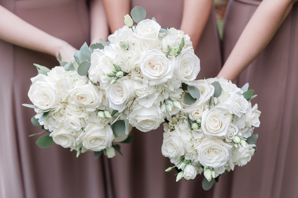 A close up of three white bridesmaids bouquets. The bridesmaids have on brown dresses.