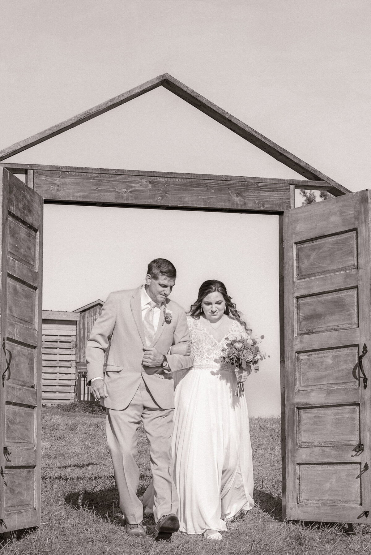 Bride walking down the aisle with her father through open wooden doors at a rustic outdoor wedding at Jerry Coopers Ranch in Pennsylvania.