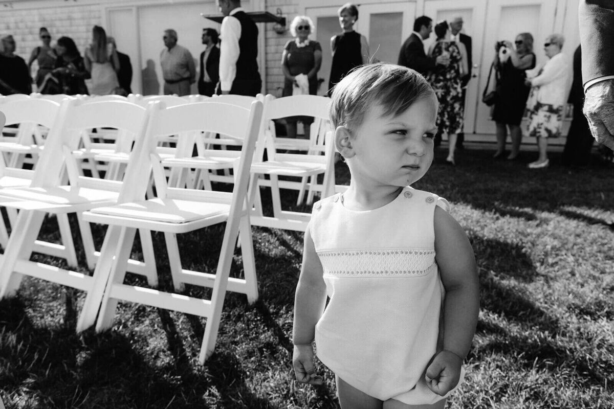 Black and white photo of a baby wearing a white onesie, ready for the wedding at Cape Cod, Osterville, MA.
