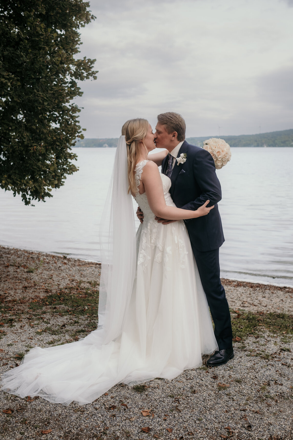 During the couple session the wedding couple kisses in front of a lake.