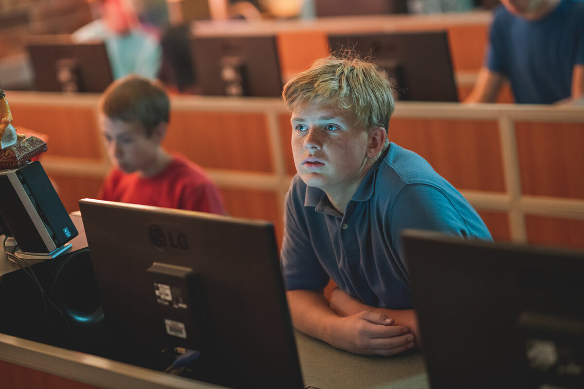 Teenage blonde male sitting in a classroom at a computer, listening to the teacher