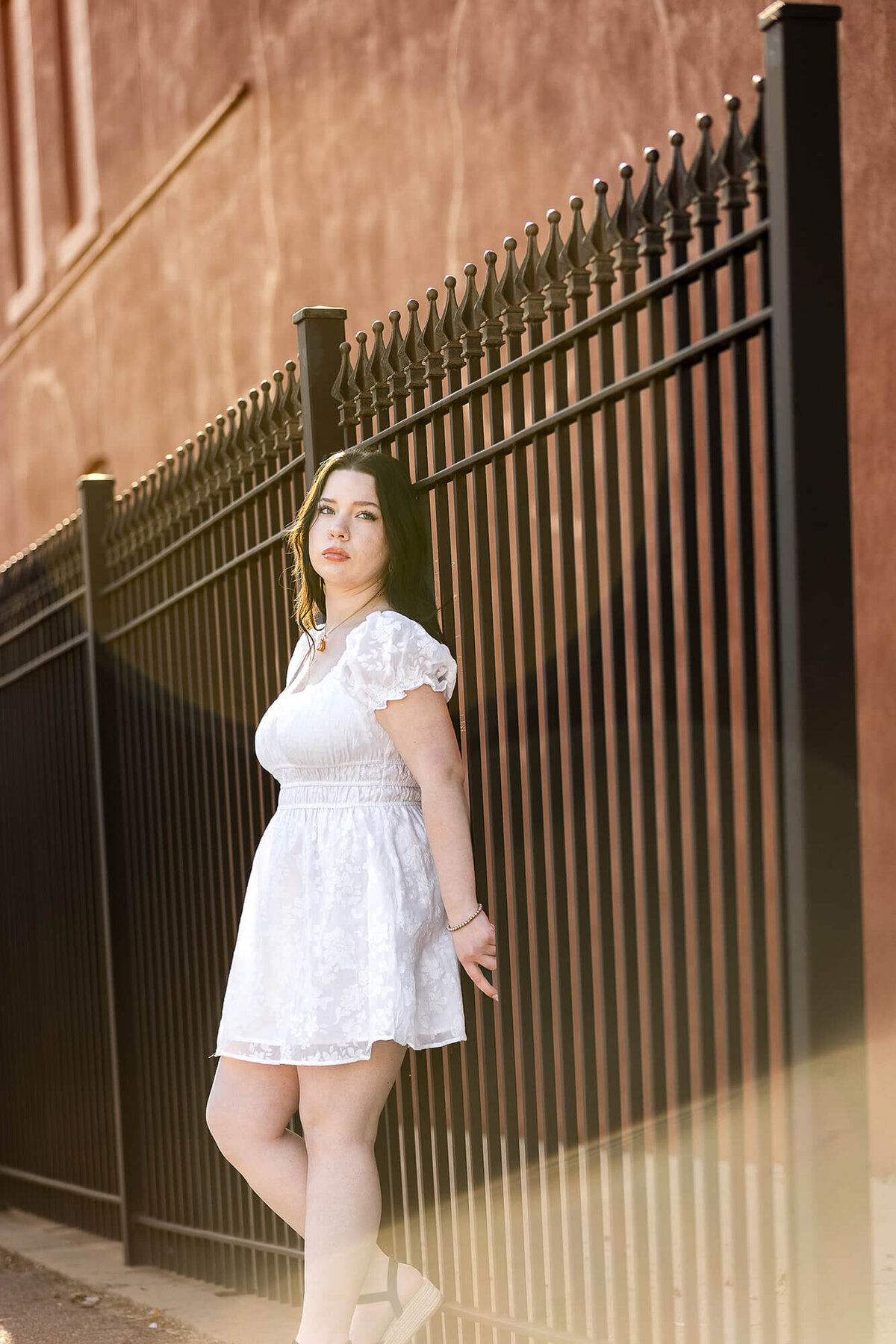 Senior girl wearing a white dress stares off into the distance during her senior photoshoot.