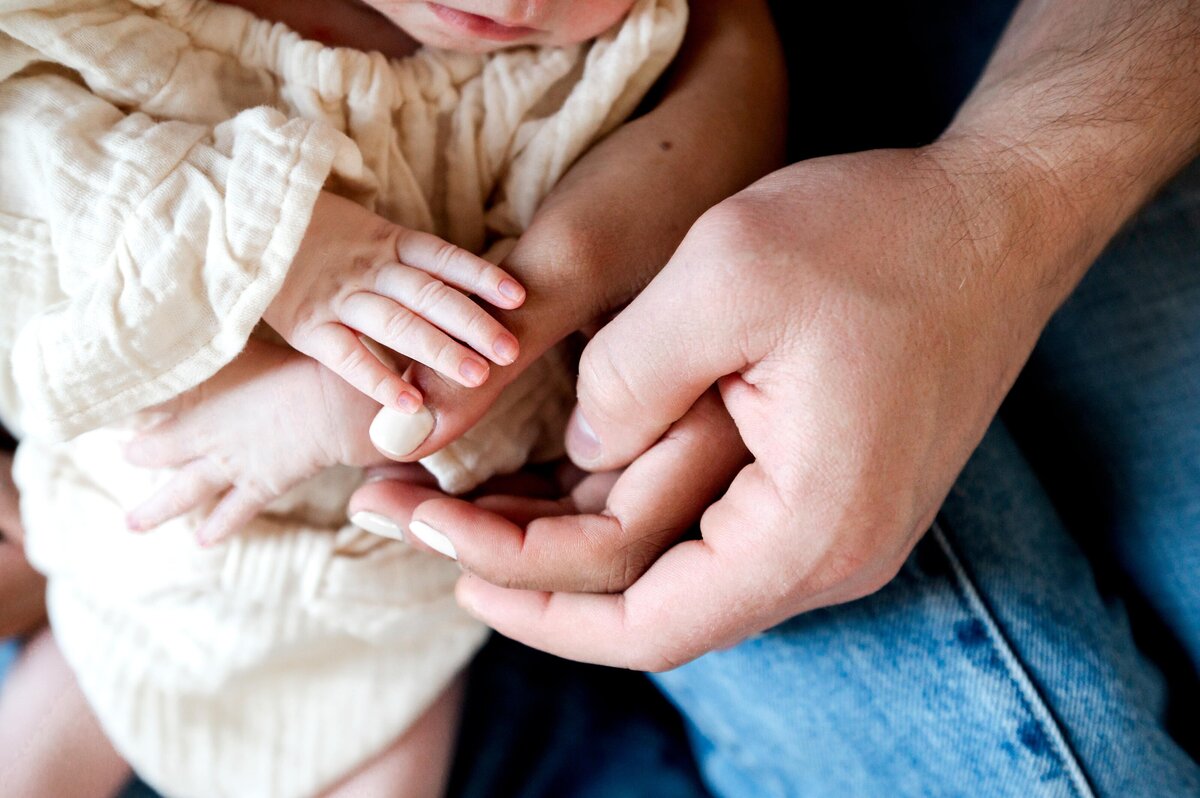 husband and wifes hands holding babys feet