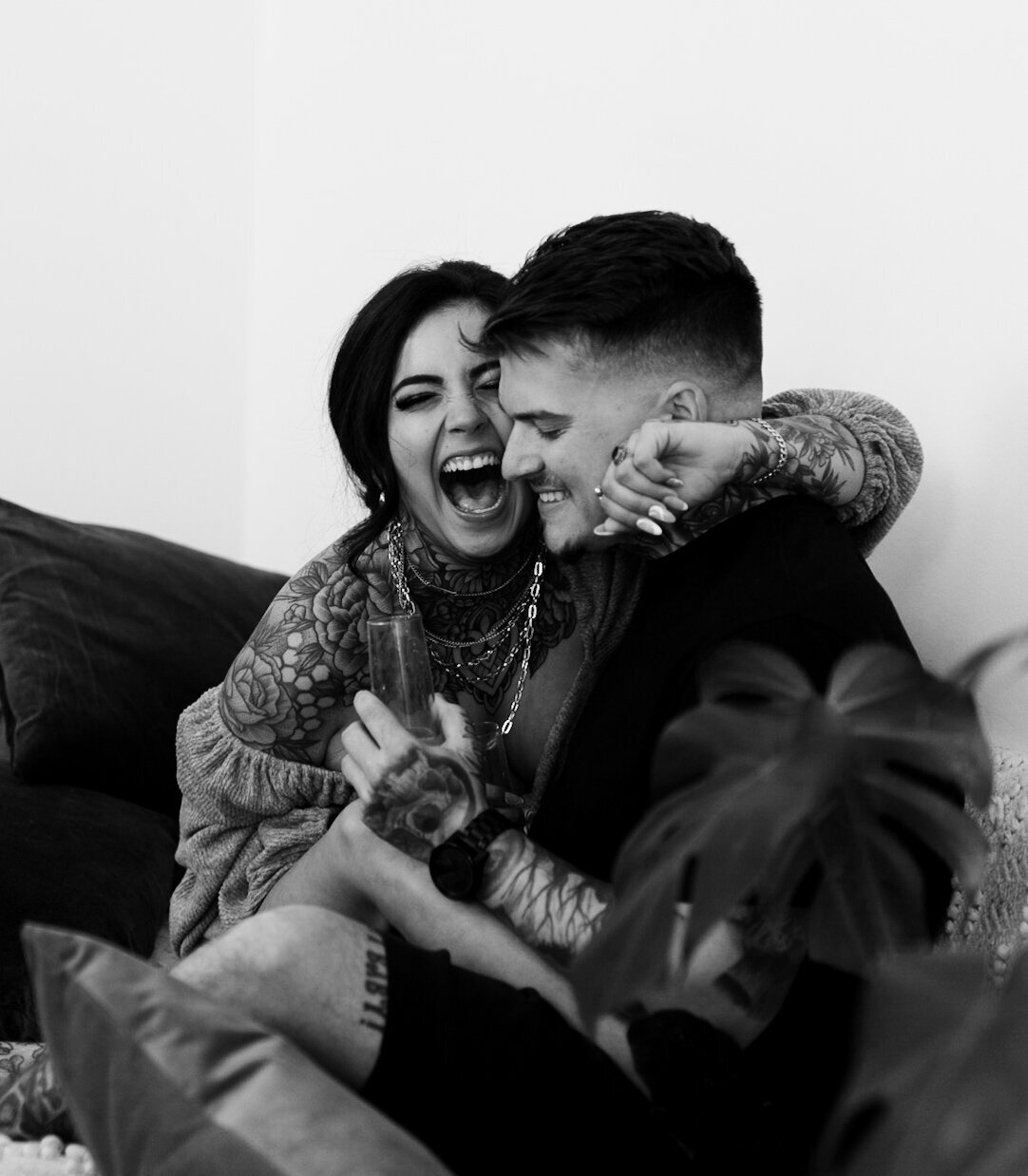 Tattooed couple holds each other and laughs at in home couples session