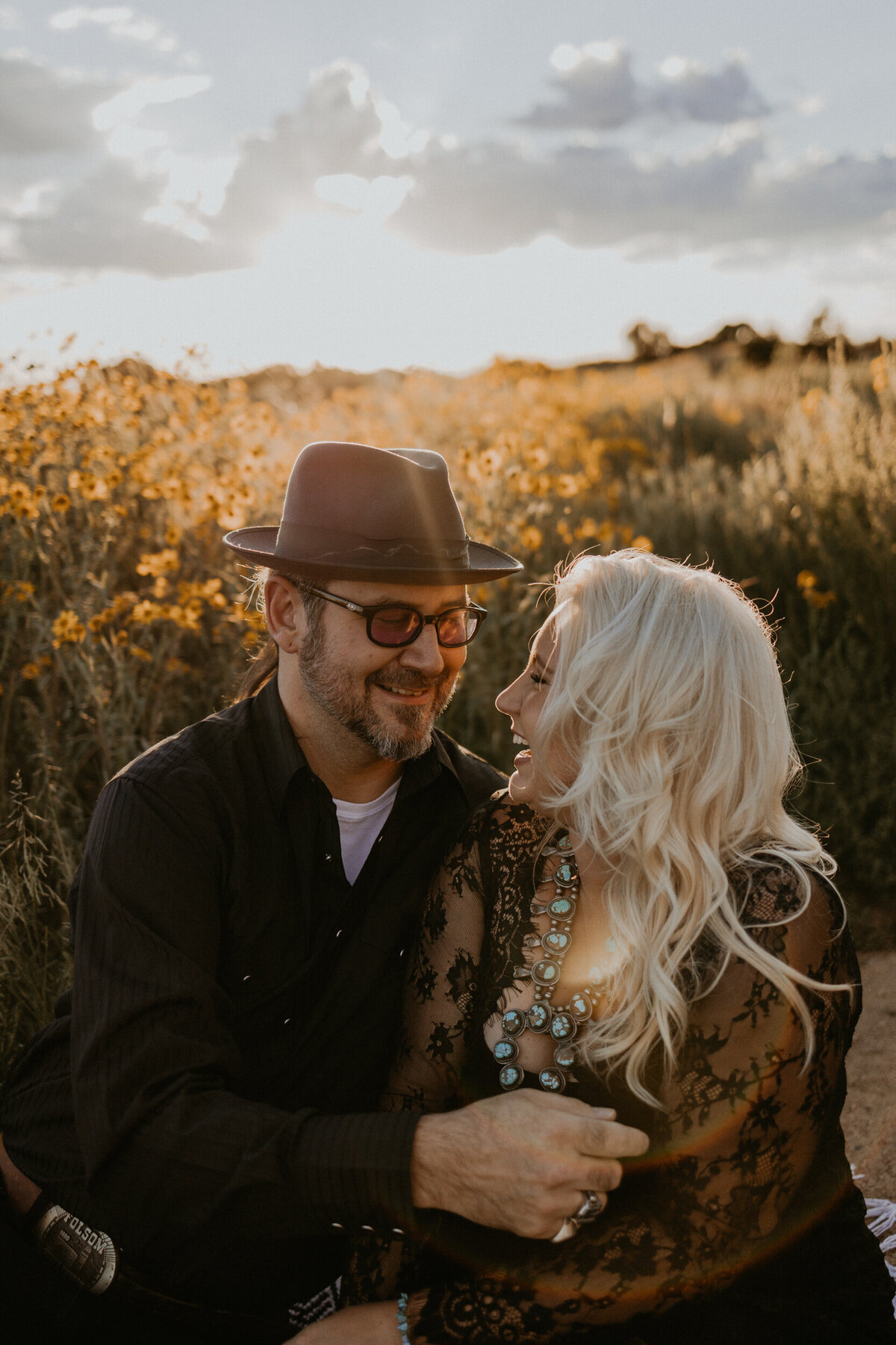 engaged couple sitting in front of wild flowers laughing