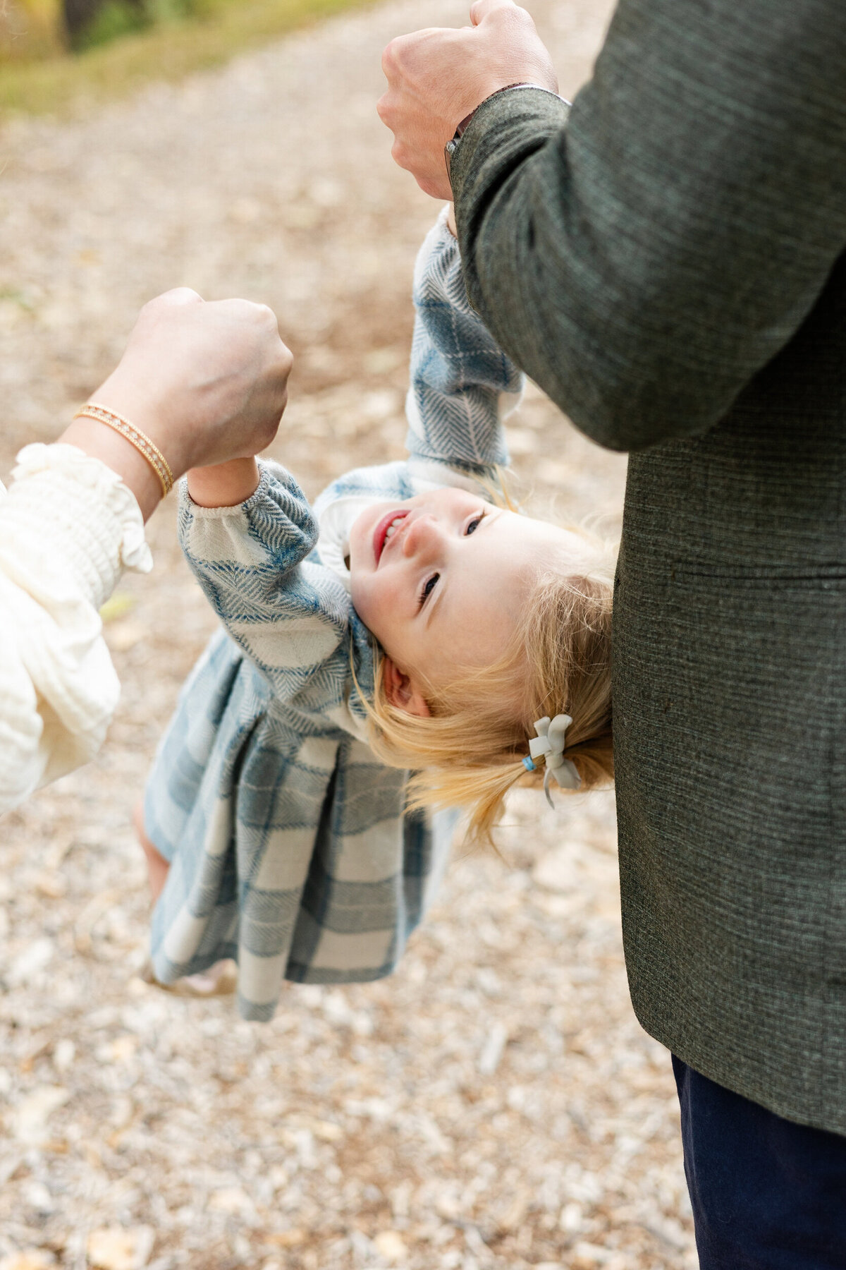 Mom and dad hold their toddler daughter's hands and swing her as she smiles.