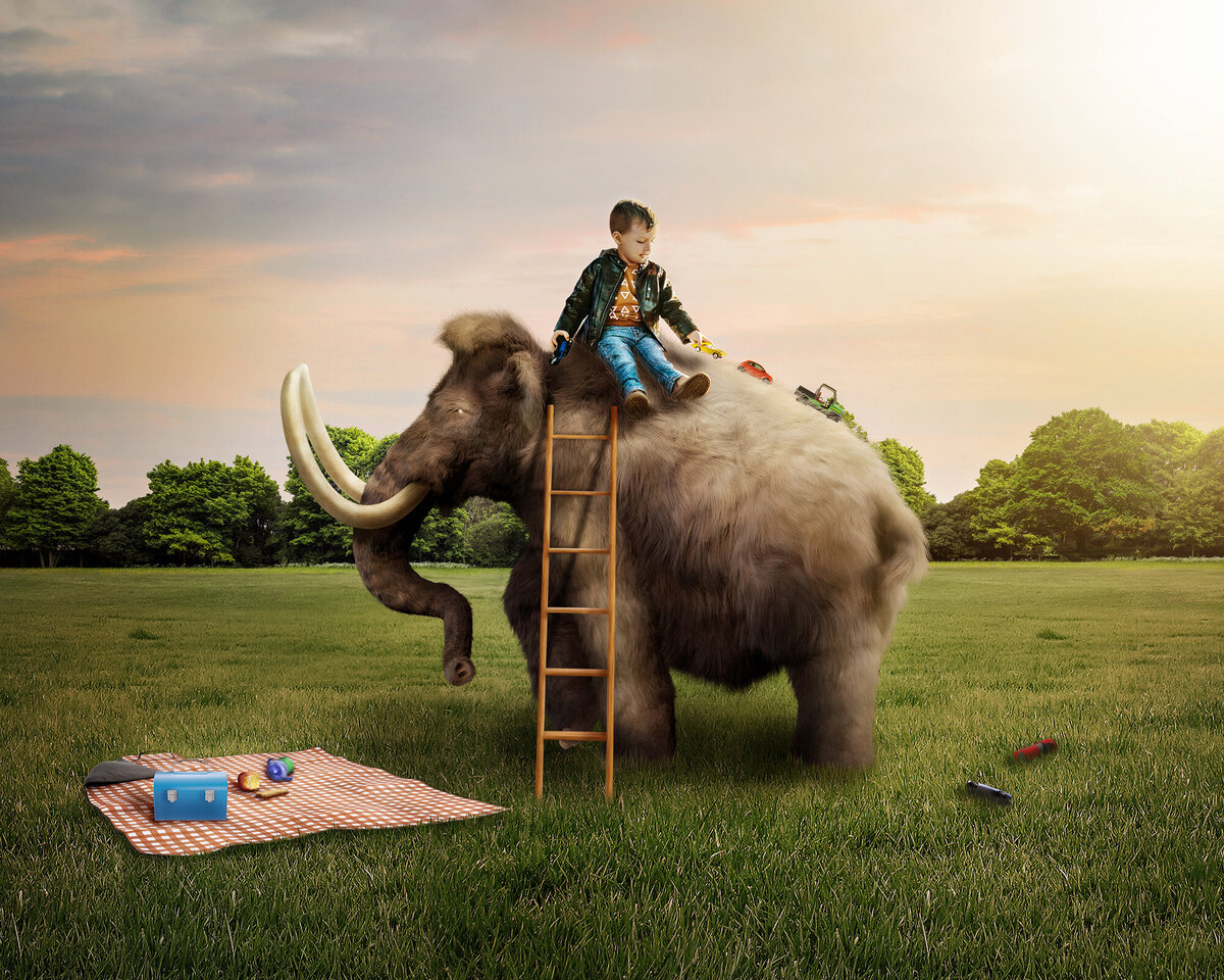 A little boy sitting on a wooly mammoth's back and playing with toy cars