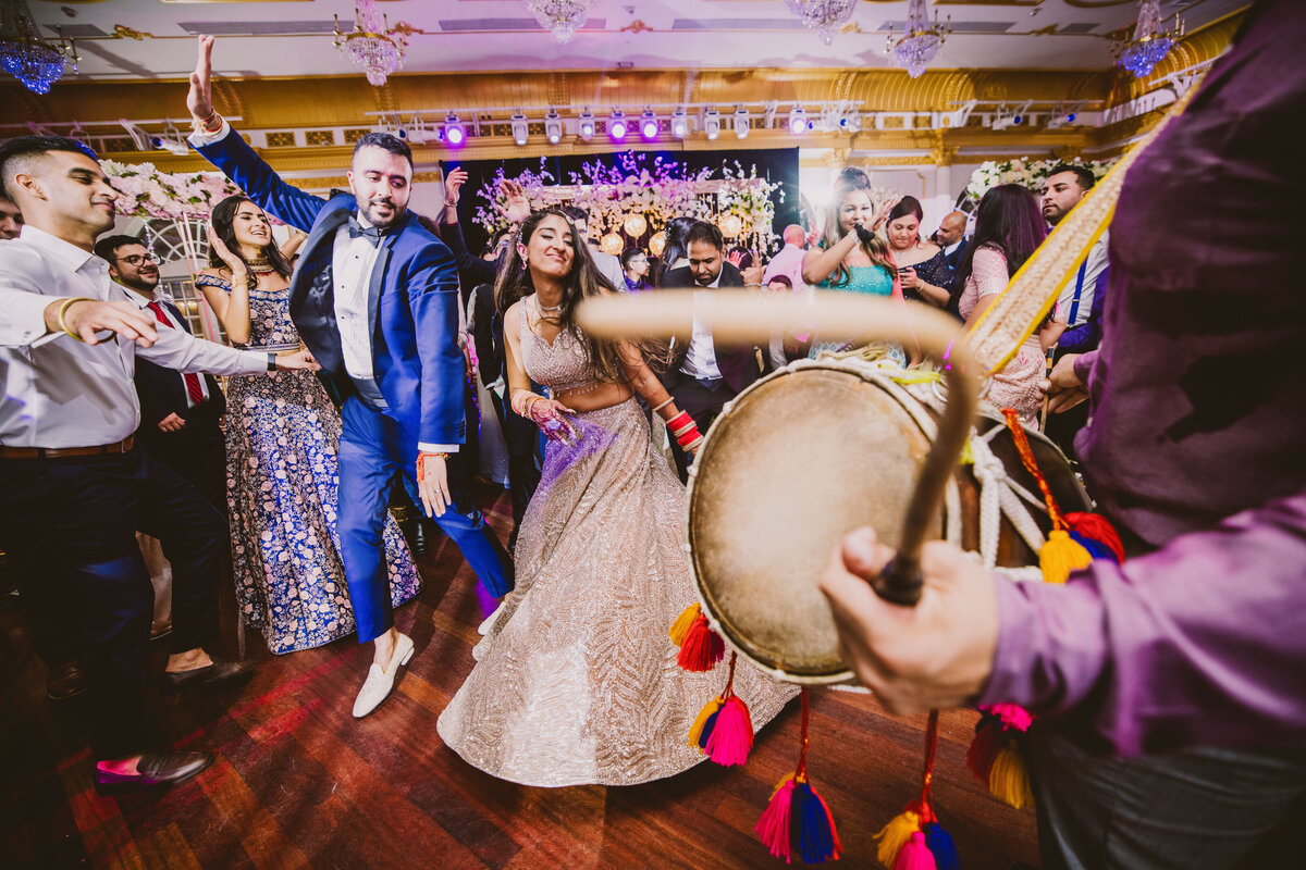 Indian hindu bride and groom dancing during the wedding reception dance floor to the dhol player