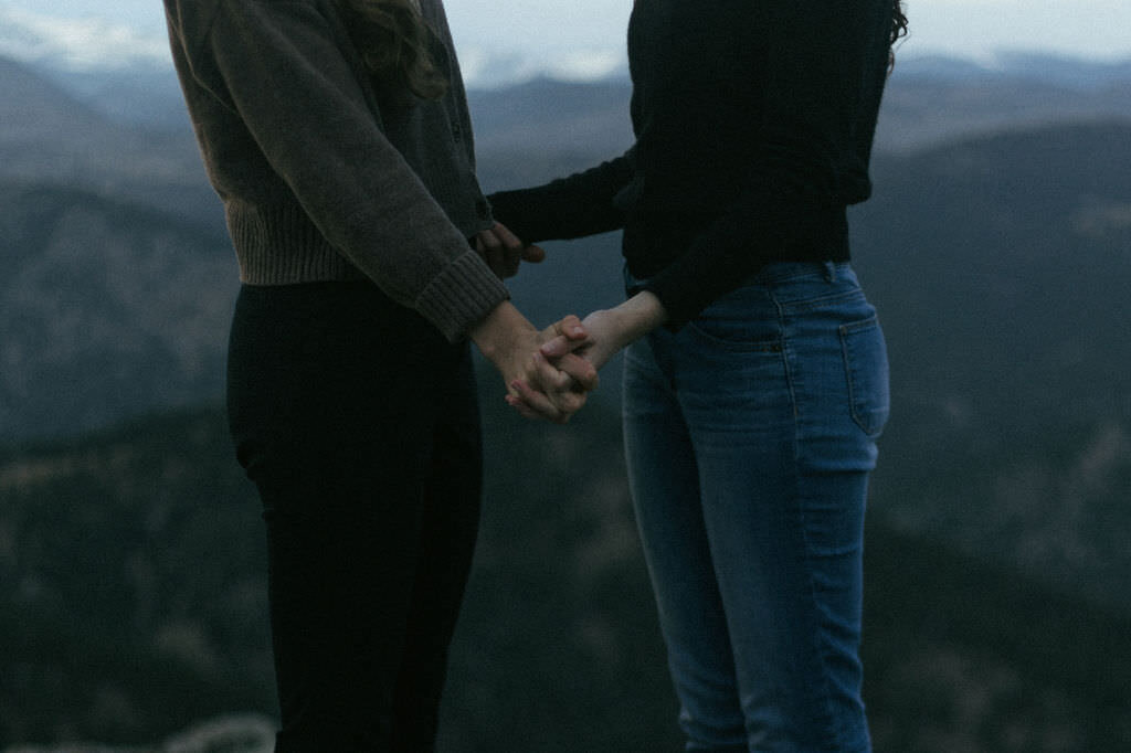 Close up of two people holding hands in the mountains.