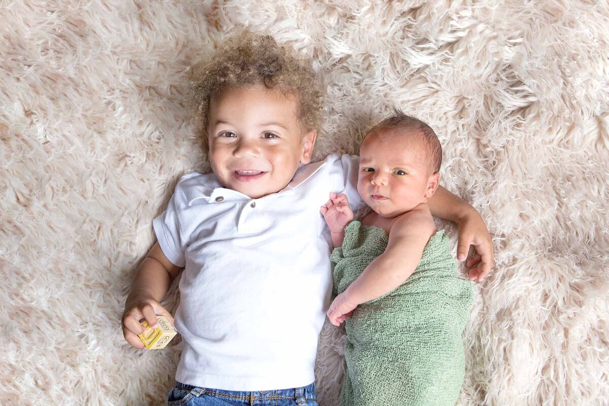 Big brother laying with newborn brother on white rug in Columbia, SC