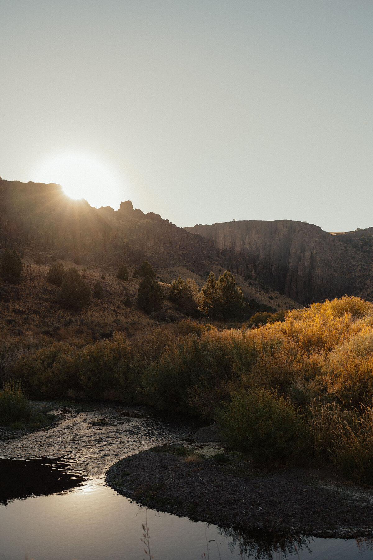 the sun shines just above the mountain horizon line with the river in the foreground in Moab, Utah