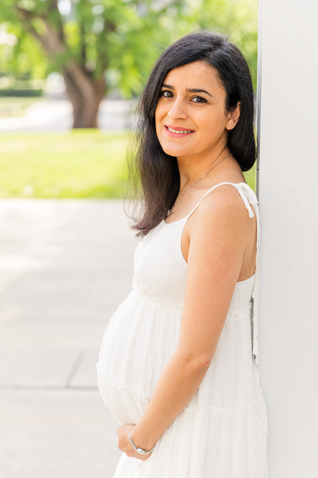 maternity pregnant woman with white dress leaning against a wall