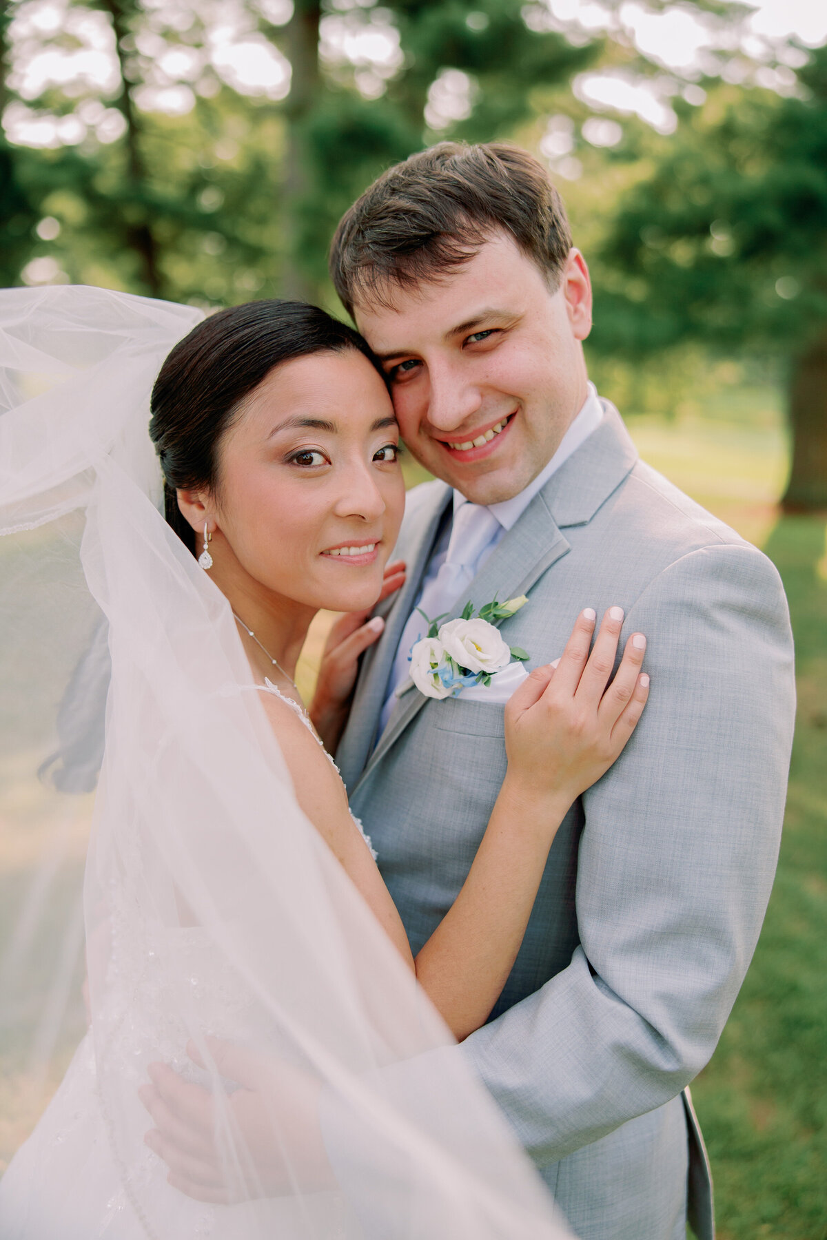 A newlywed couple standing close together, head to head, as they smile 