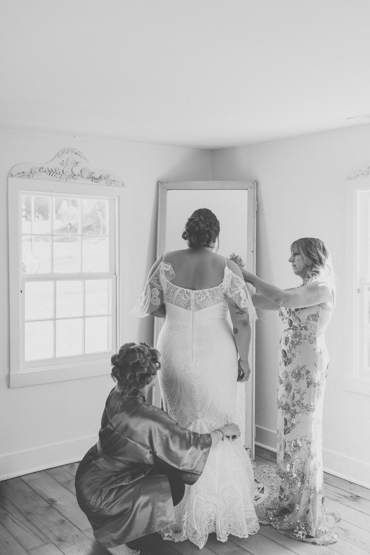 Black and white photo of bride’s mother helping fasten gown before wedding ceremony at Carolina Home and Garden.