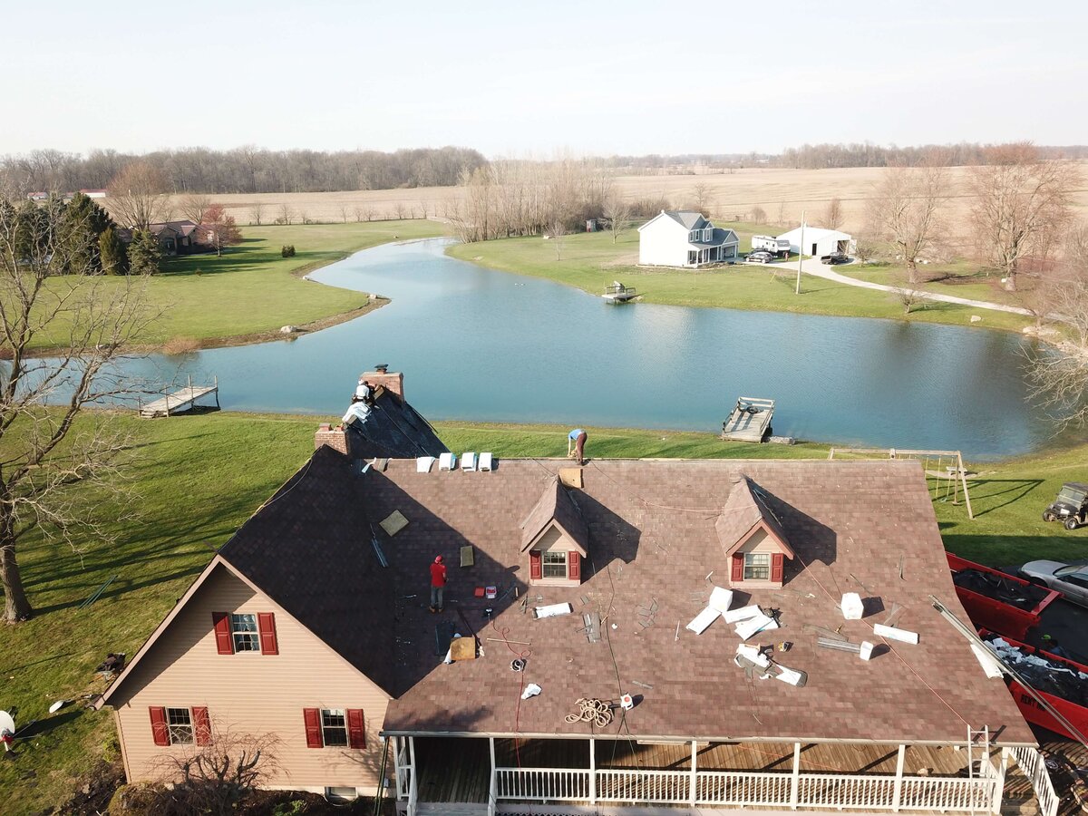 Black Bear Roofing team working on a roof near a scenic pond in a rural area.