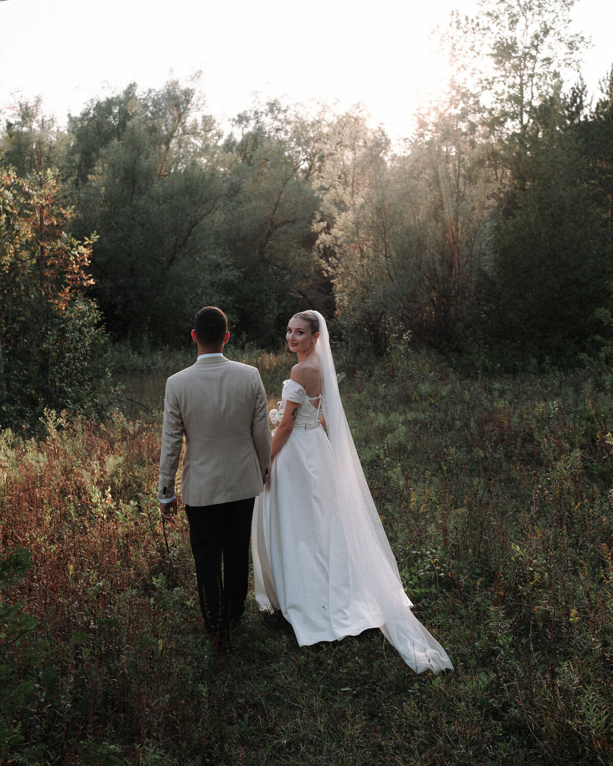 newlyweds walking through nature as she looks back at me