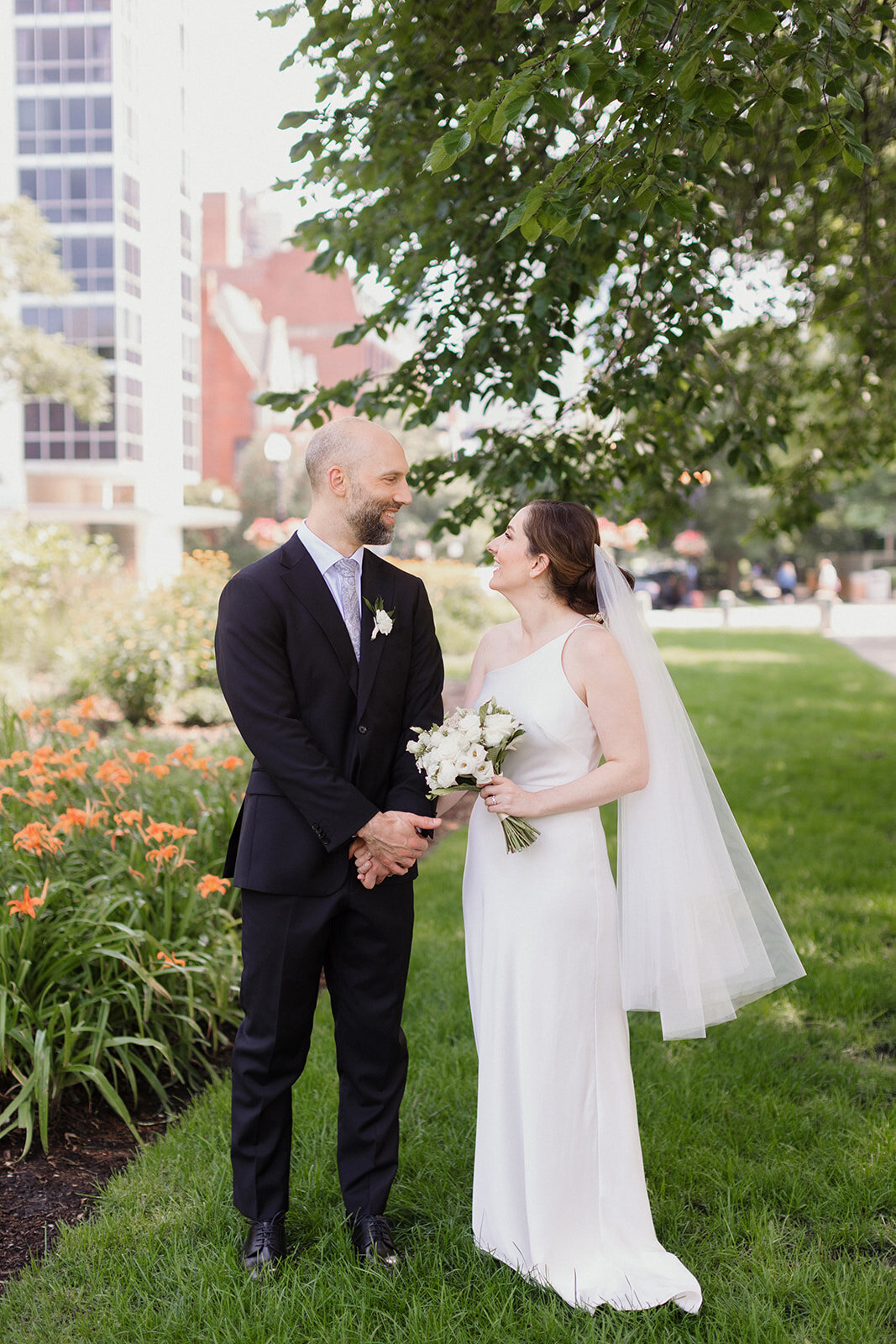 couple walks through garden holding hands and sharing a happy moment as they look at one another