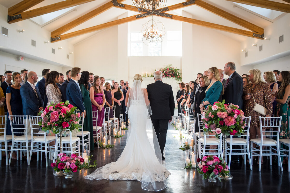 A wide angle shot of a bride and her father walking up the aisle at The Oaks at Plum Creek.